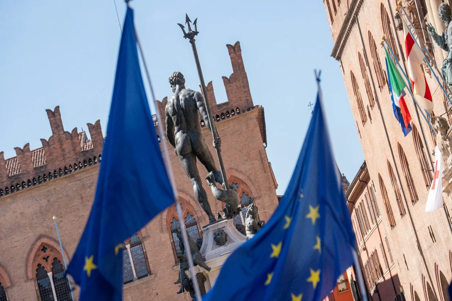 Immaggine della città di bologna, in particolare della statua del Nettuno e di un palazzo di Piazza Maggiore con bandiere dell'Europa. 
