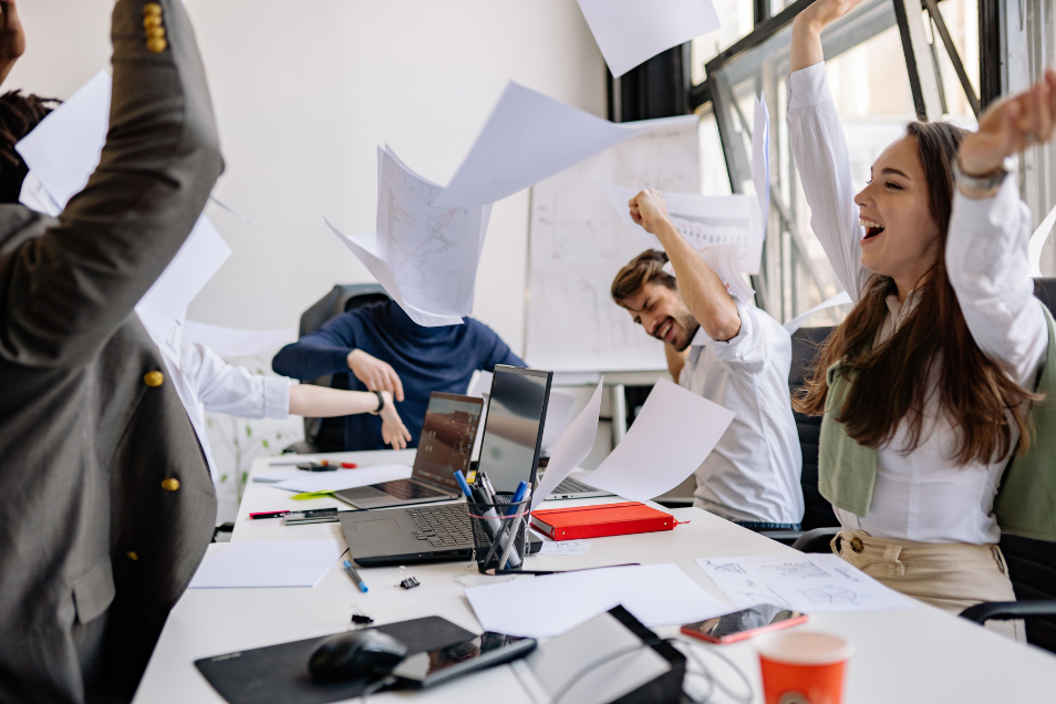 persone in un ufficio con dei computer che lanciano felicemente dei fogli in giro