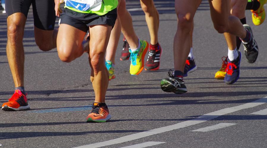 Foto di persone che corrono viste dalle gambe in giù. Piedi che corrono su strada asfaltata.