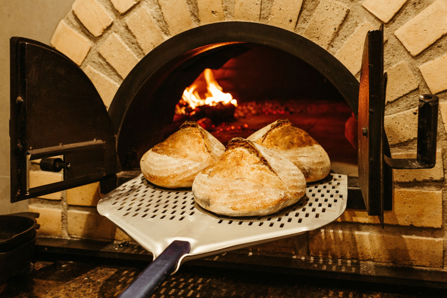 Tre pagnotte di pane a lievitazione naturale cuociono in un forno di mattoni rustico, mostrando l'artigianato culinario tradizionale.