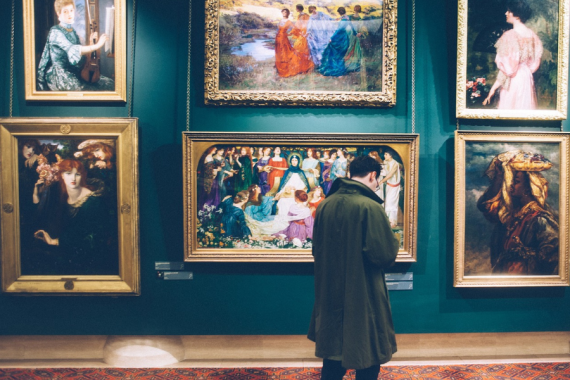 uomo in un museo di fronte a quadri 