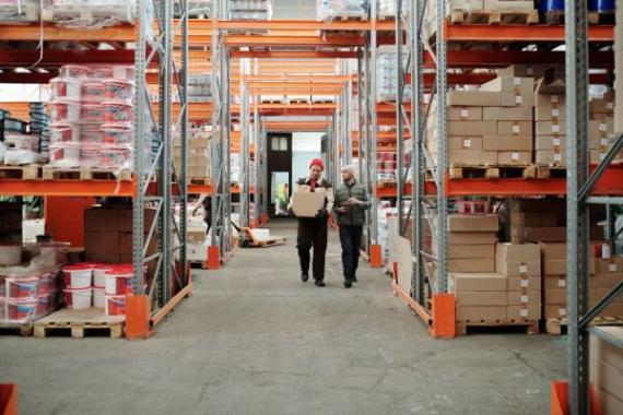 Due lavoratori gestiscono un pacco in un ampio magazzino circondato da scaffali pieni di scatole e prodotti