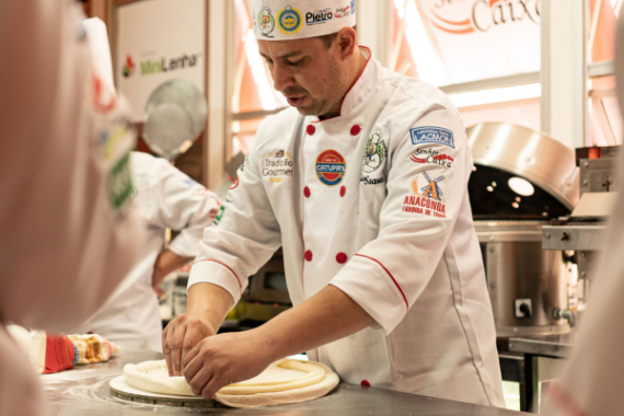 Chef che lavora l'impasto in una cucina professionale, mostrando abilità culinarie e dettagli dell'uniforme.